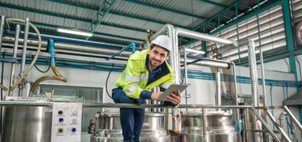 Caucasian technician engineer man in uniform with tablet checking and control boiler tanks and liquid pipeline in chemical factory production line